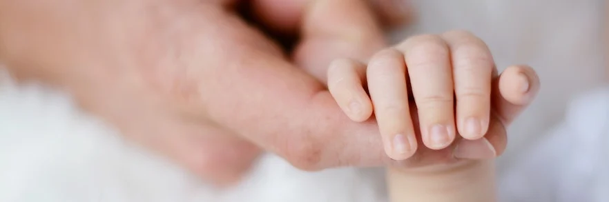 Finger von Elternteil in Hand von einem Baby