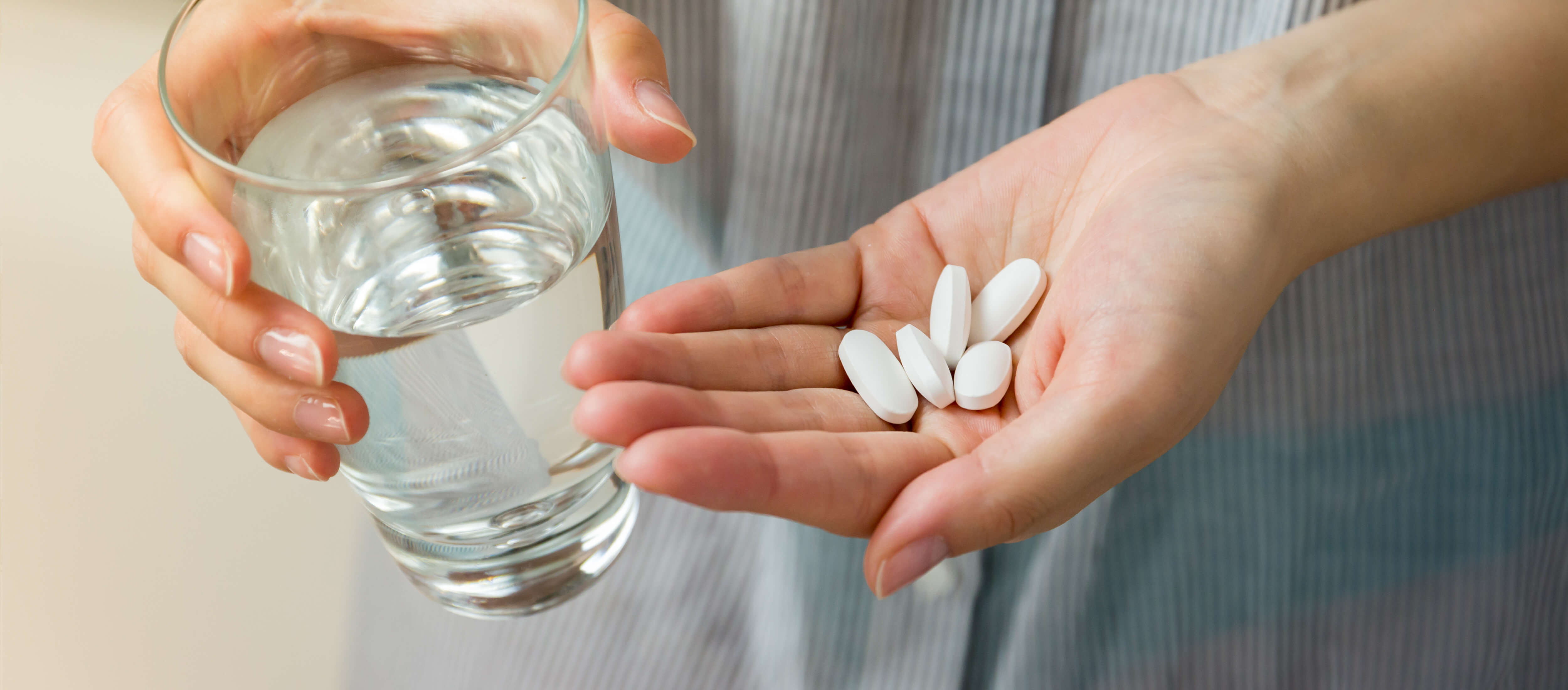 Tabletten und Glas Wasser in Händen